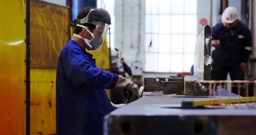 Worker Grinding Metal with Protective Gear in Factory