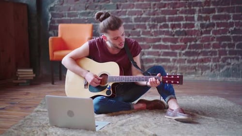 Young Adult Plays Guitar with Laptop in Urban Setting