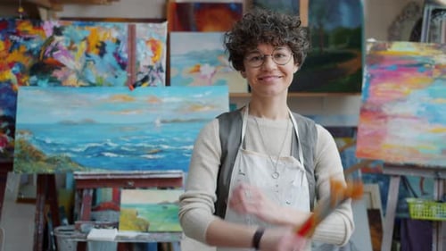 Smiling Woman Artist with Paintings and Paintbrushes