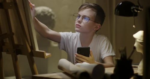Boy Drawing on Canvas While Using Phone for Reference