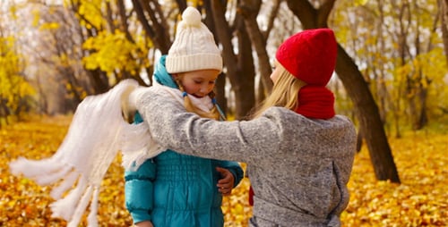 Mother Tying Scarf on Child in Autumn Park