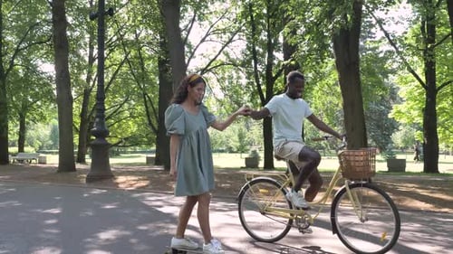 Black Man Rides Bike Holding Brunette Hand Riding Skateboard