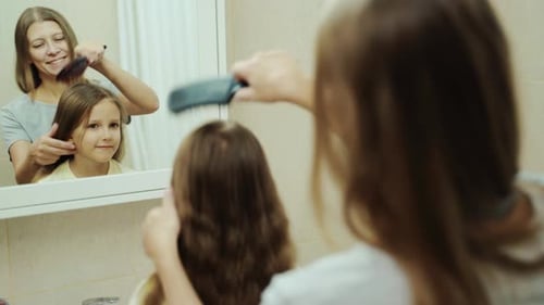 Mother brushing child's long brown hair in bathroom