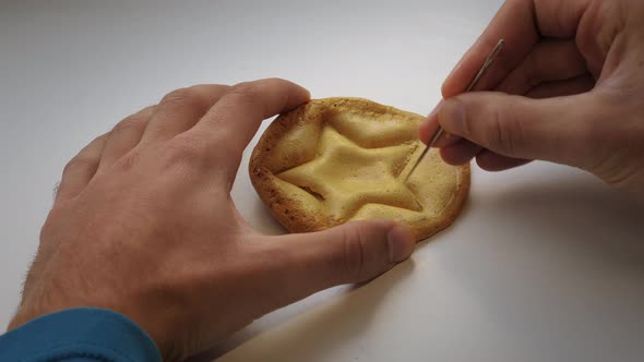 Cover for Squid Game. Hands scratching brown caramel Dalgona candy with needle, close up.