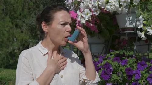 Woman Uses Inhaler Outdoors Near Flowers