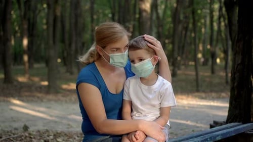 Mother Hugs Her Son in Medical Masks While Sitting in a Park