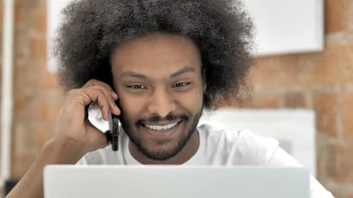 Smiling Young Adult Talking on Phone with Laptop