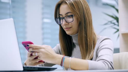 Female Office Worker Uses Phone While Working on Laptop Plays Mobile Game Break