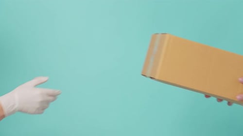 Close up of delivery man wearing hand glove holding parcel box in hands and giving to customer.