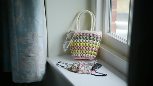 Woman grabbing cute bag and puts items in to leave house, face mask with flower pattern, sunny windo
