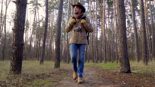 A Man with Camera Walks Along a Trail in the Forest
