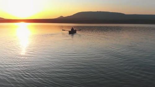 Mann segelt auf dem Boot mit Paddeln auf dem Fluss während des Sonnenuntergangs