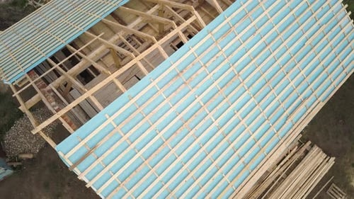 Aerial view of a brick house with wooden roof frame under construction.