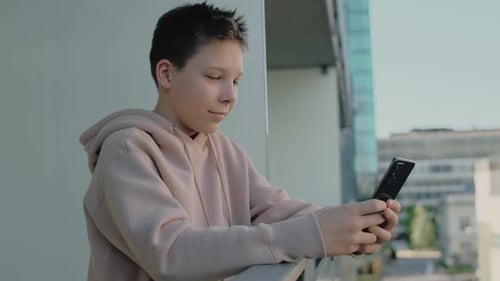 Teen Using Smartphone on Balcony in the City