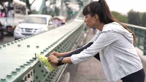 4K Hispanic woman stretching her leg while jogging in the city at summer sunset.
