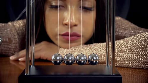 Woman Watches Newton's Cradle Swing Back and Forth