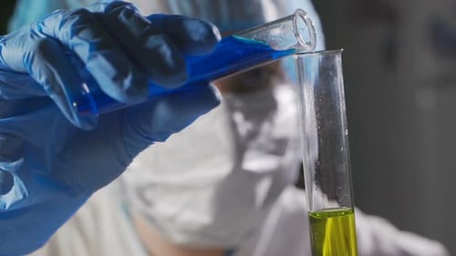 Scientist Mixing Blue and Yellow Liquids in Test Tubes