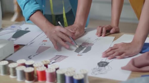 Close Up Of Male And Female Designers Hands Designing Clothes On The Paper In The Studio