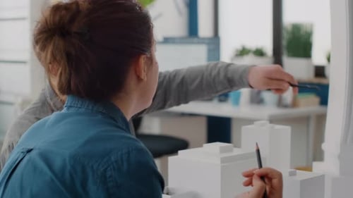 Close Up of Man and Woman Talking About Maquette Design Analyzing Blueprints Plans on Table