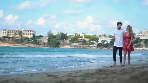 Young Couple Holding Hands Walking Towards Sunset on Empty Beach Speaking with Each Other