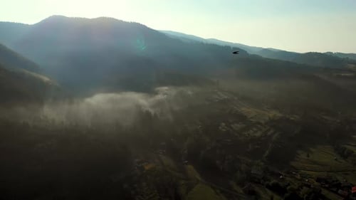 Luftaufnahme des Sonnenaufgangs über einem nebligen Dorf in den Bergen.