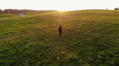 Aerial Footage of a Young Girl Running Through a Green Meadow with Her Arms Raised Towards the