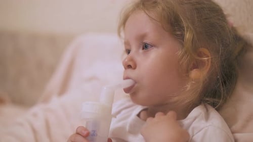 Une fille bouclée subit une intervention avec un inhalateur pour le rhume au lit