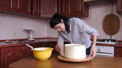 Woman Smooths Frosting on Cake in Kitchen