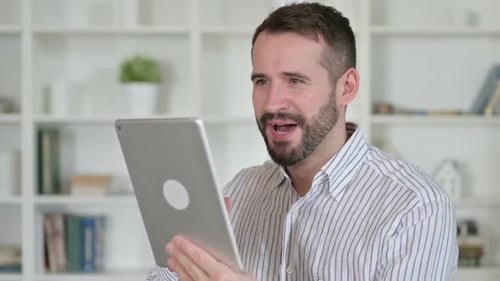 Bearded Man Smiling While Using Tablet Indoors