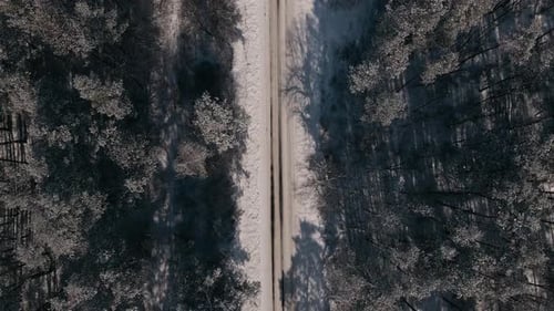 Vue aérienne du haut vers le bas Drone vol à reculons au-dessus de la petite route rurale et de la forêt par une journée ensoleillée d'hiver