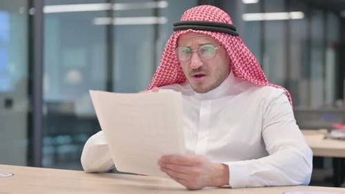 Man in Headscarf Reviews Document in Office