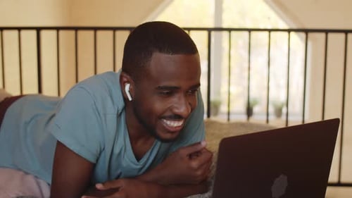 Man Video Conferencing on Laptop While Lying in Bed