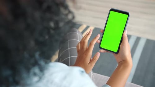 Vista posterior de una mujer morena usando la pantalla táctil de un teléfono inteligente con pantalla verde