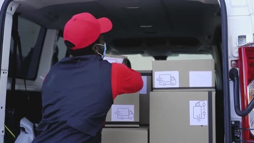 Afrikanischer Zusteller lädt Kisten in den LKW, während er eine Gesichtsmaske trägt