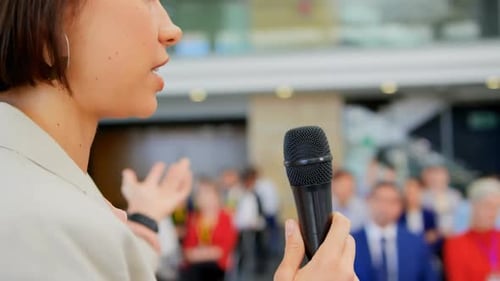 Young Woman Speaks at Business Conference with Microphone