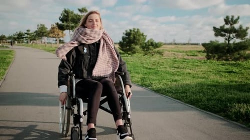 Woman with Disease of Legs and Spine Is Riding Wheelchair in Park Smiling