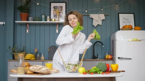 Cheerful Young Woman Dancing With Green Salad In Kitchen