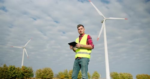 Der Ingenieur arbeitet mit dem Tablet in der Hand neben den Windmühlenturbinen