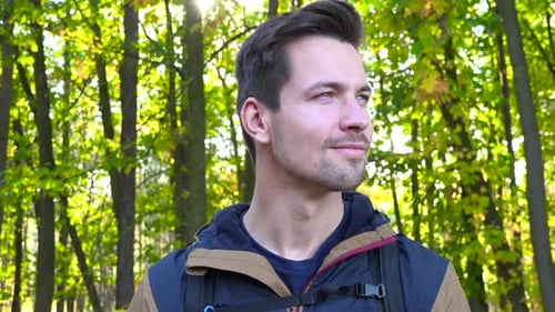 Ein junger gutaussehender Backpacker schaut sich mit einem Lächeln im Wald um - Nahaufnahme von unten