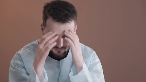 Male in Medical Gown Rubbing Temples