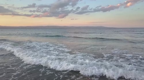 Aerial view of a sea surface with blue water waves under sunset sky.