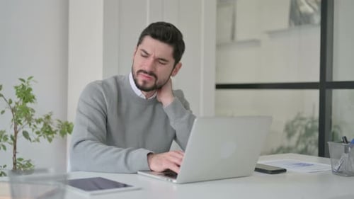 Young Man Having Neck Pain While Using Laptop in Office