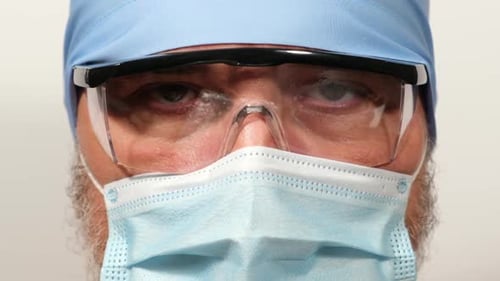 Arzt in einer Textilkappe, durchsichtige Schutzbrille