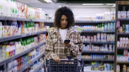 African American with Shopping Cart Using Smartphone at Supermarket