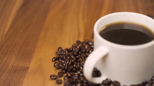 Steaming Coffee Cup Surrounded by Roasted Coffee Beans