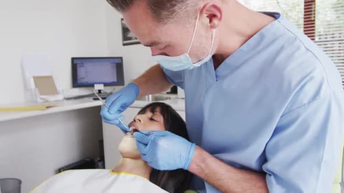 Caucasian male dentist with face mask examining teeth of female patient at modern dental clinic