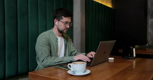 Young Adult Works on Laptop at Cafe Table
