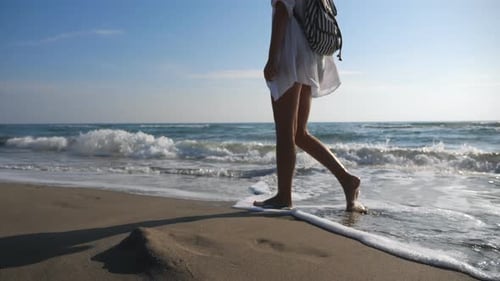 Attractive Woman with Backpack Strolling Across Sandy Beach and Admiring Beautiful View
