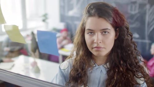 Young Caucasian Girl Arranging Sticky Notes on Glass Wall in Office