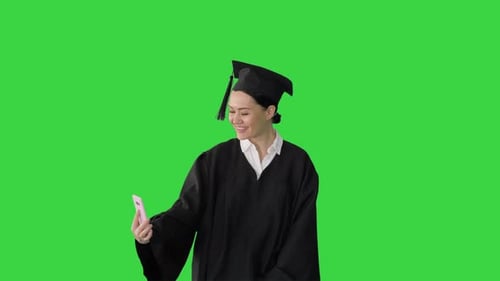 Happy Female Graduate in Mortarboard Making Selfie on Her Phone on a Green Screen, Chroma Key